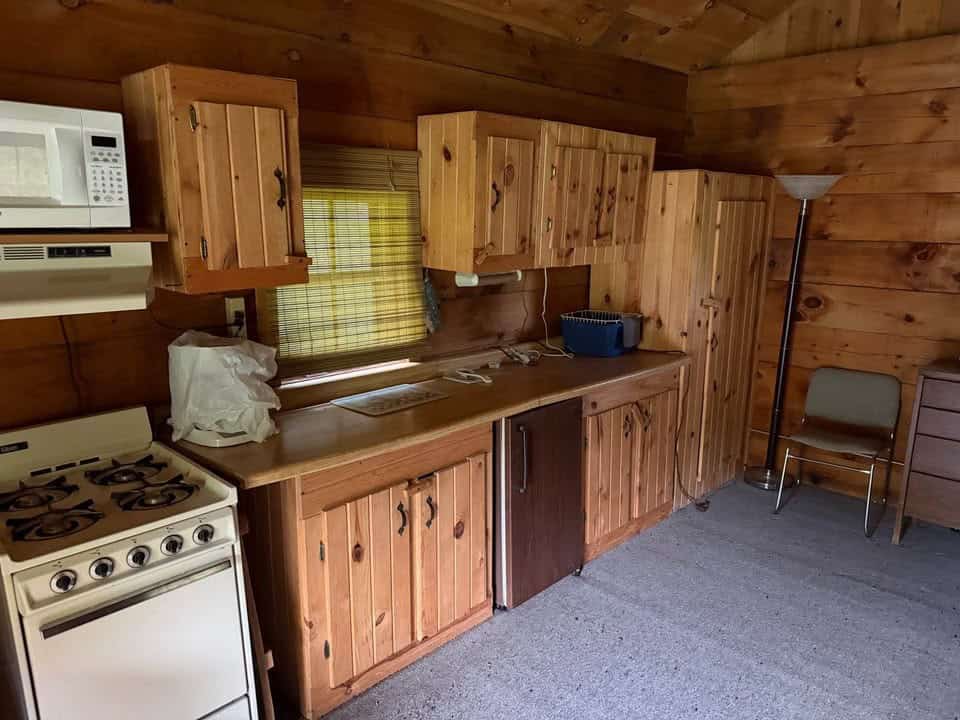 Knotty pine kitchenette with a white gas stove, microwave, sink, and small refrigerator