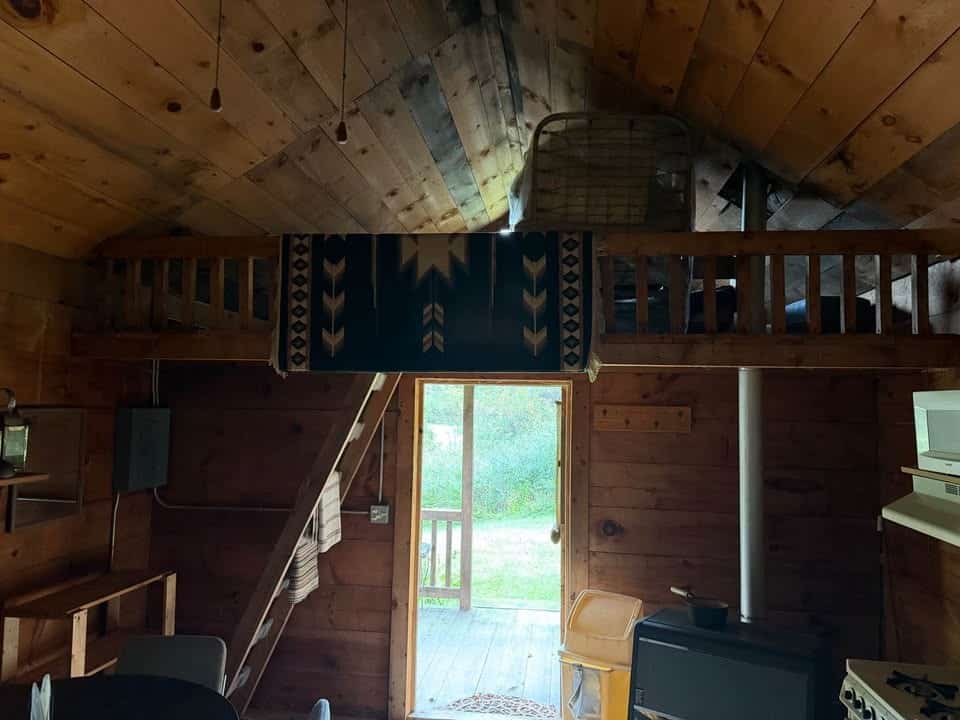 Sleeping loft with a log railing above the entry door and a ladder up the wall