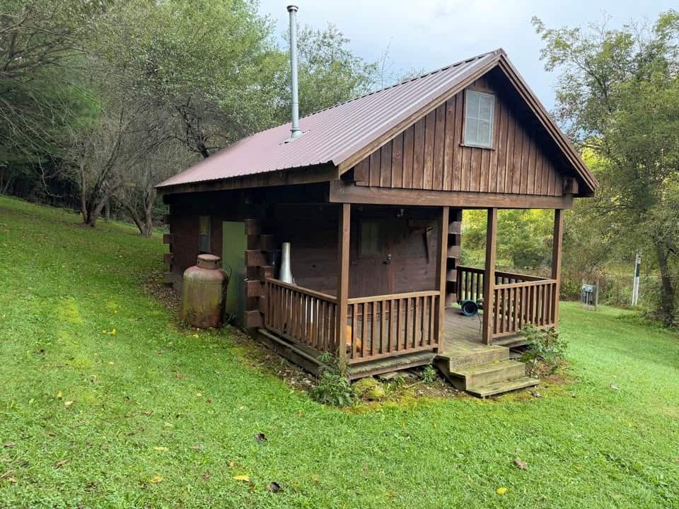 Side and porch of the log cabin with a propane tank and stovepipe