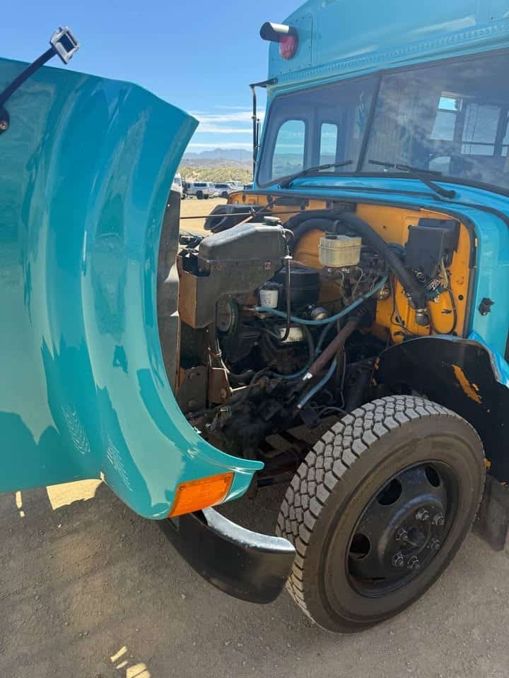 Hood tilted open on the teal bus, showing the 7.3 diesel engine and front tire