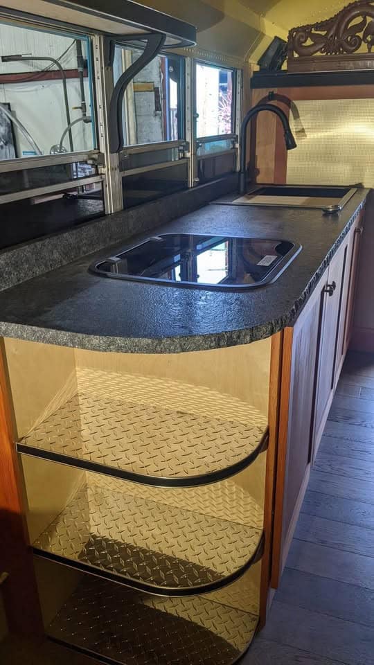 Galley with black granite countertop, flush-mount stove, and wood cabinetry along the bus wall