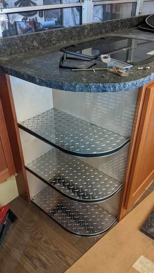 Curved corner shelves with diamond-plate liners under the granite counter