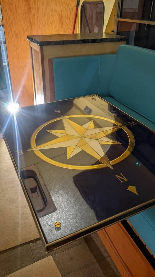 Black fold-down table with a gold compass rose inlay over the teal bench