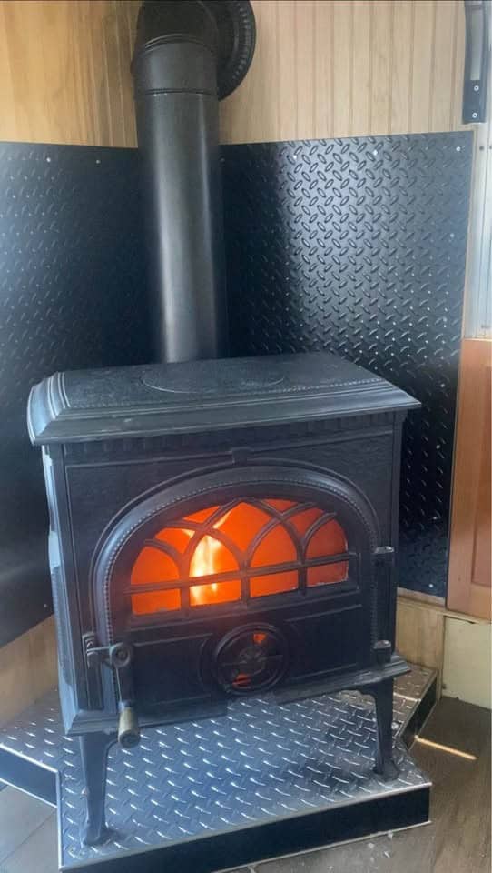 Small Jotul cast-iron wood stove with a lit fire, set on a diamond-plate hearth