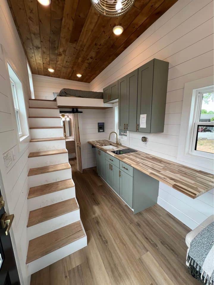 Compact tiny house kitchen with modern cabinetry and a cozy loft sleeping area.
