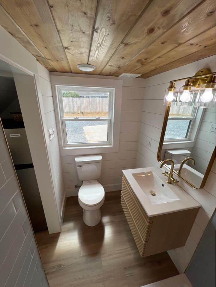 Small farmhouse bathroom with wooden ceiling, white walls, and modern fixtures.