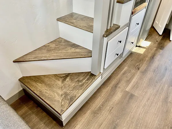 Tiny house stairs with wood finish and white cabinetry.