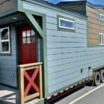 Charming tiny house on wheels with colorful exterior and small porch, perfect for minimalist living.