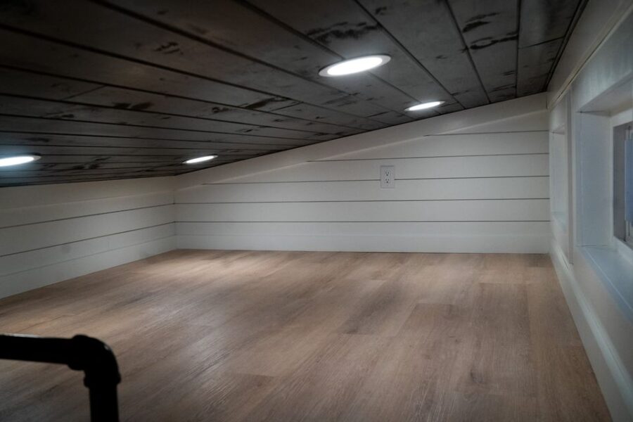 Lofted tiny house space with white shiplap walls and wooden flooring.