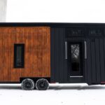 Compact tiny house on wheels with a black exterior and wooden accent wall, suitable for small space.