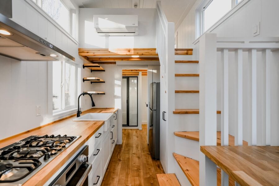 Compact tiny house kitchen with white cabinets and wooden countertops.