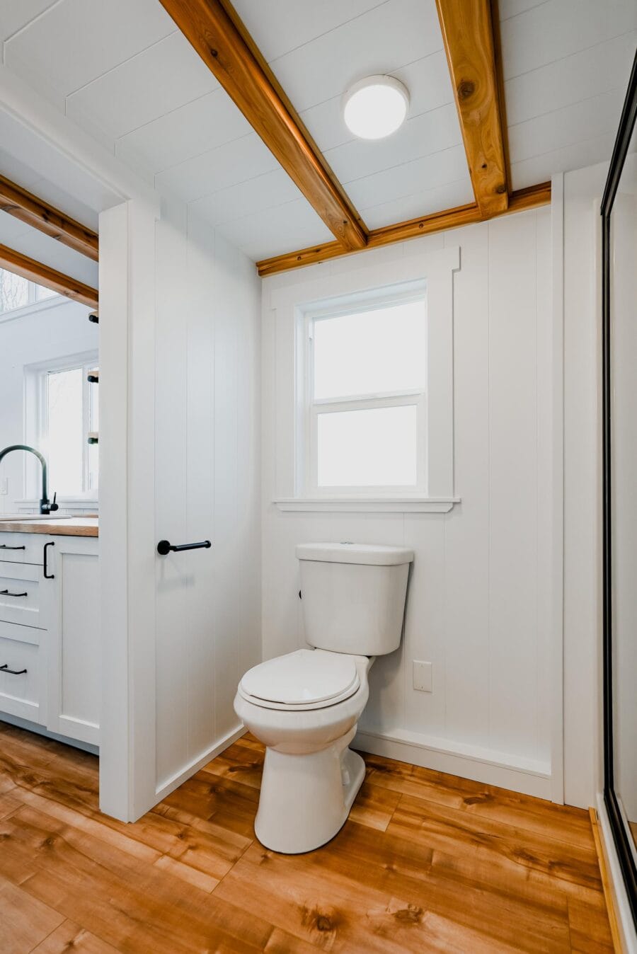 Bright tiny house bathroom with white walls and natural wood accents.