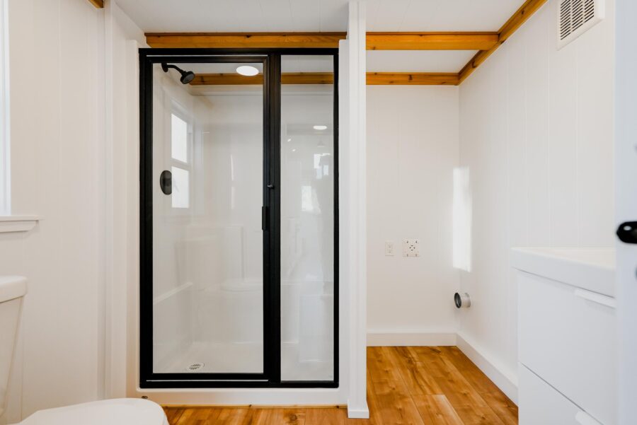 Interior view of a compact tiny house shower with glass door and minimalist design.