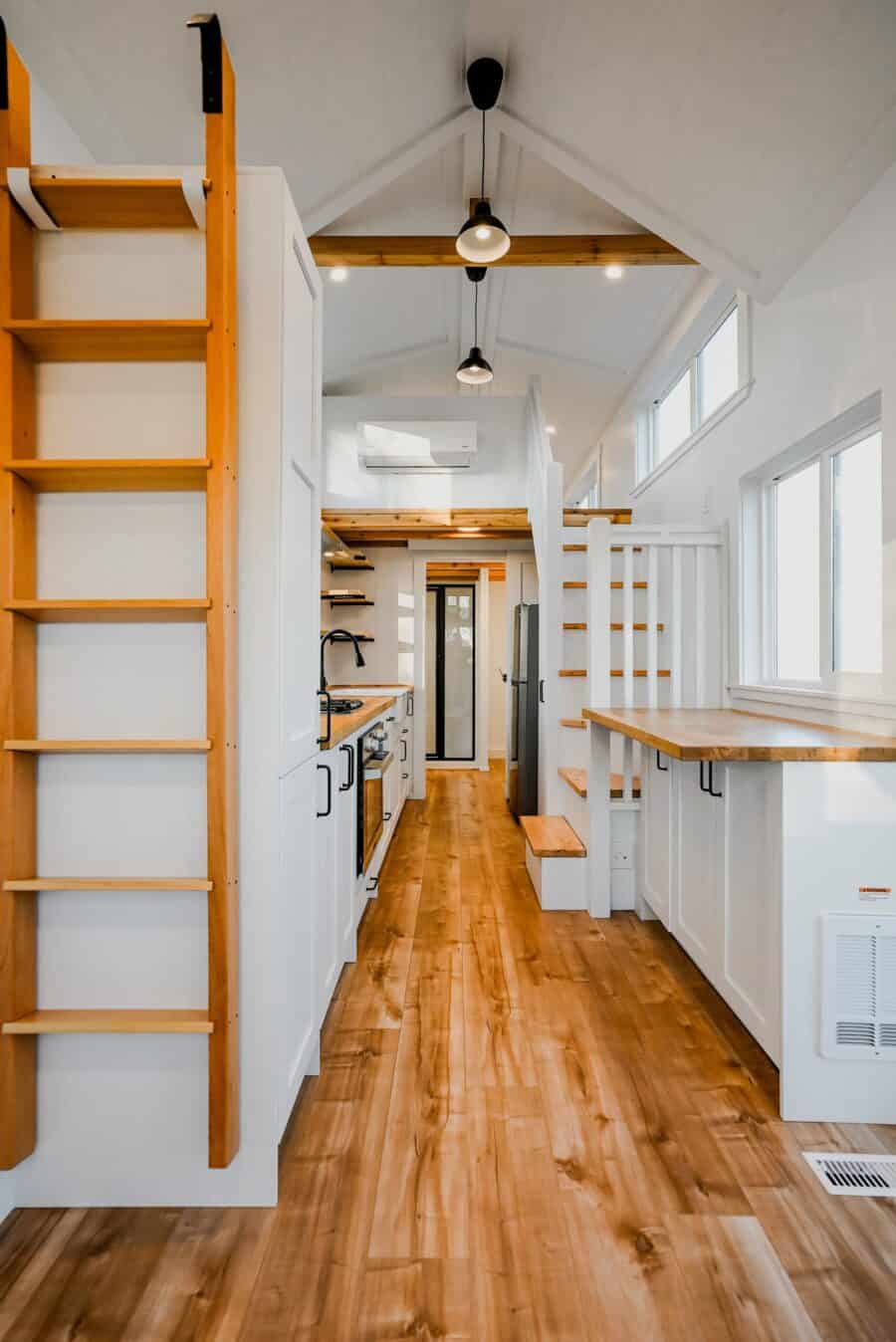 Bright tiny house interior with loft, wooden floors, and large windows for natural light.