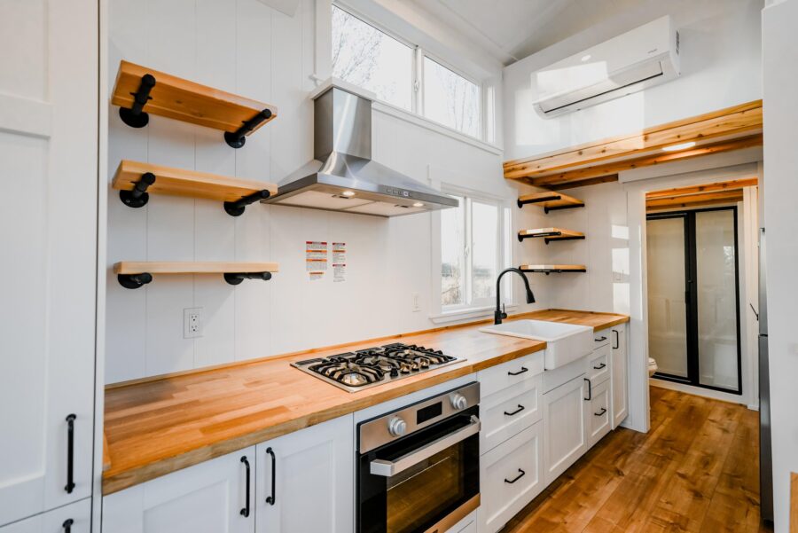 Compact tiny house kitchen with white cabinets and wooden countertops.