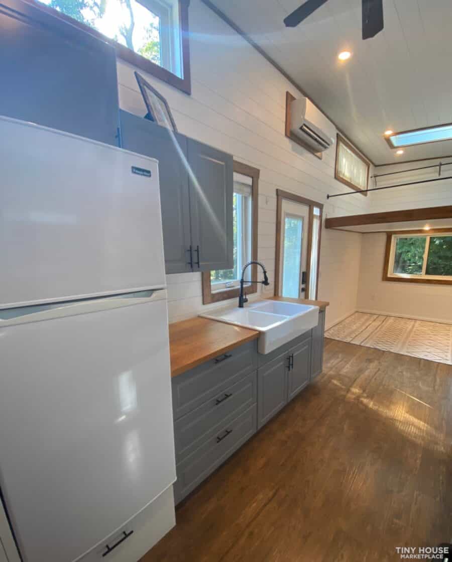 Cozy tiny house kitchen with white cabinets, wooden countertops, and large windows in a modern farmh.