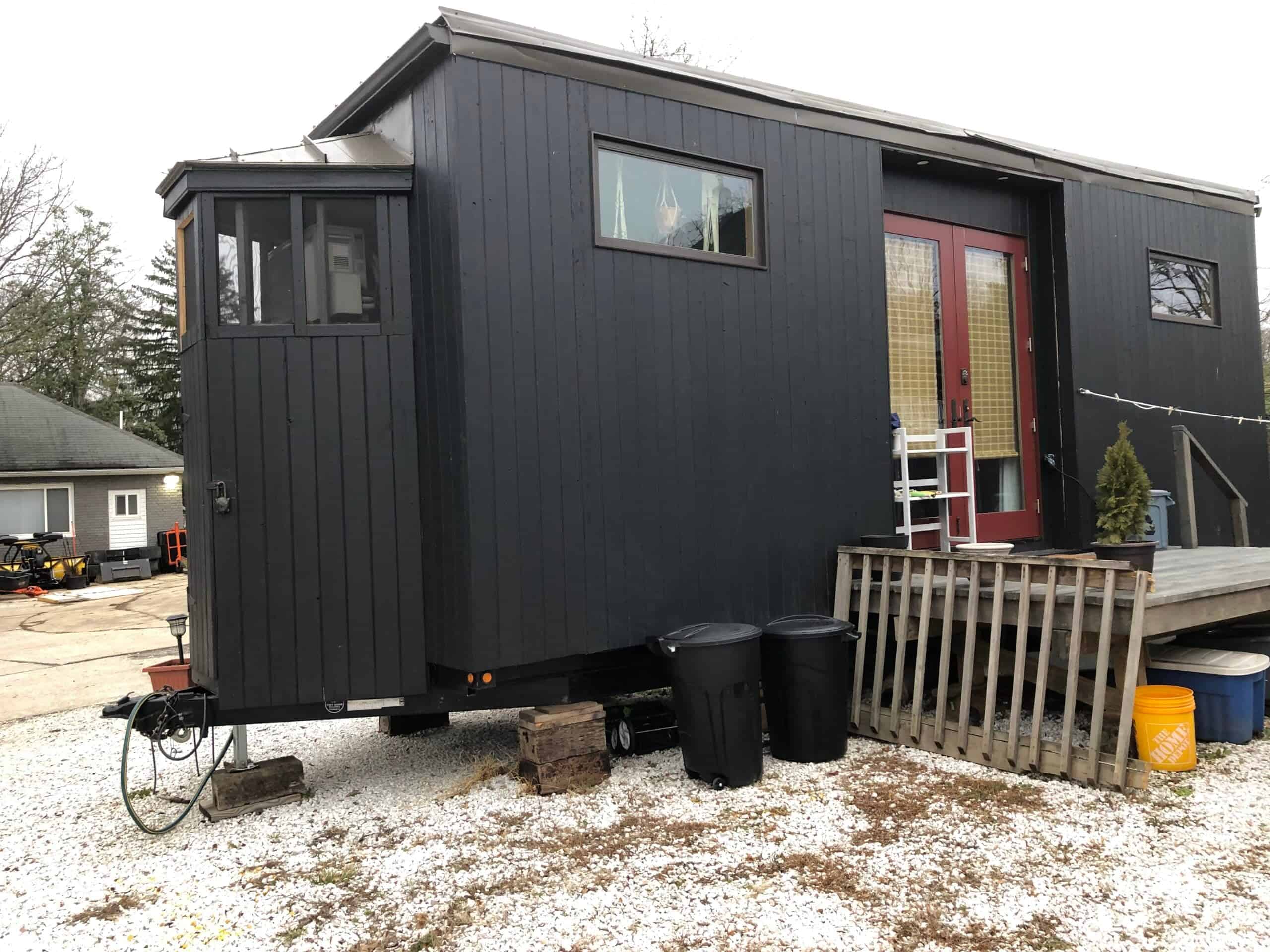 All-black tiny house with a red door, featuring a Murphy bed and modern design.