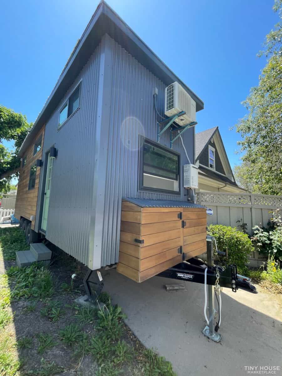 Tiny House with sleek metal exterior and wooden accents, set in a lush green yard.