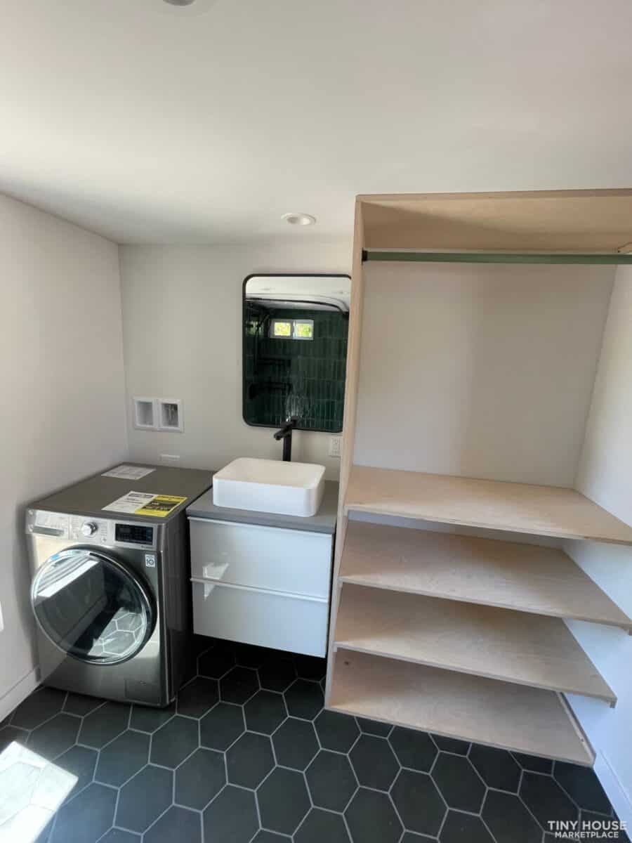 Tiny house laundry and storage area with washer, sink, and open shelving.