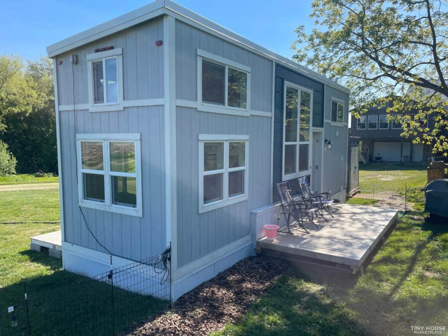 Bright blue tiny house with large windows and a small deck, designed for work and living in a compac.