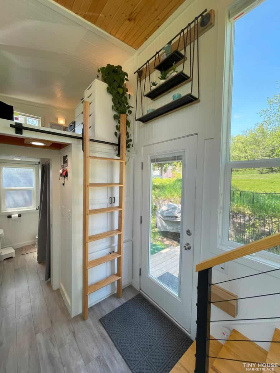 Entryway of a tiny house featuring a ladder leading to a loft and large windows for natural light.