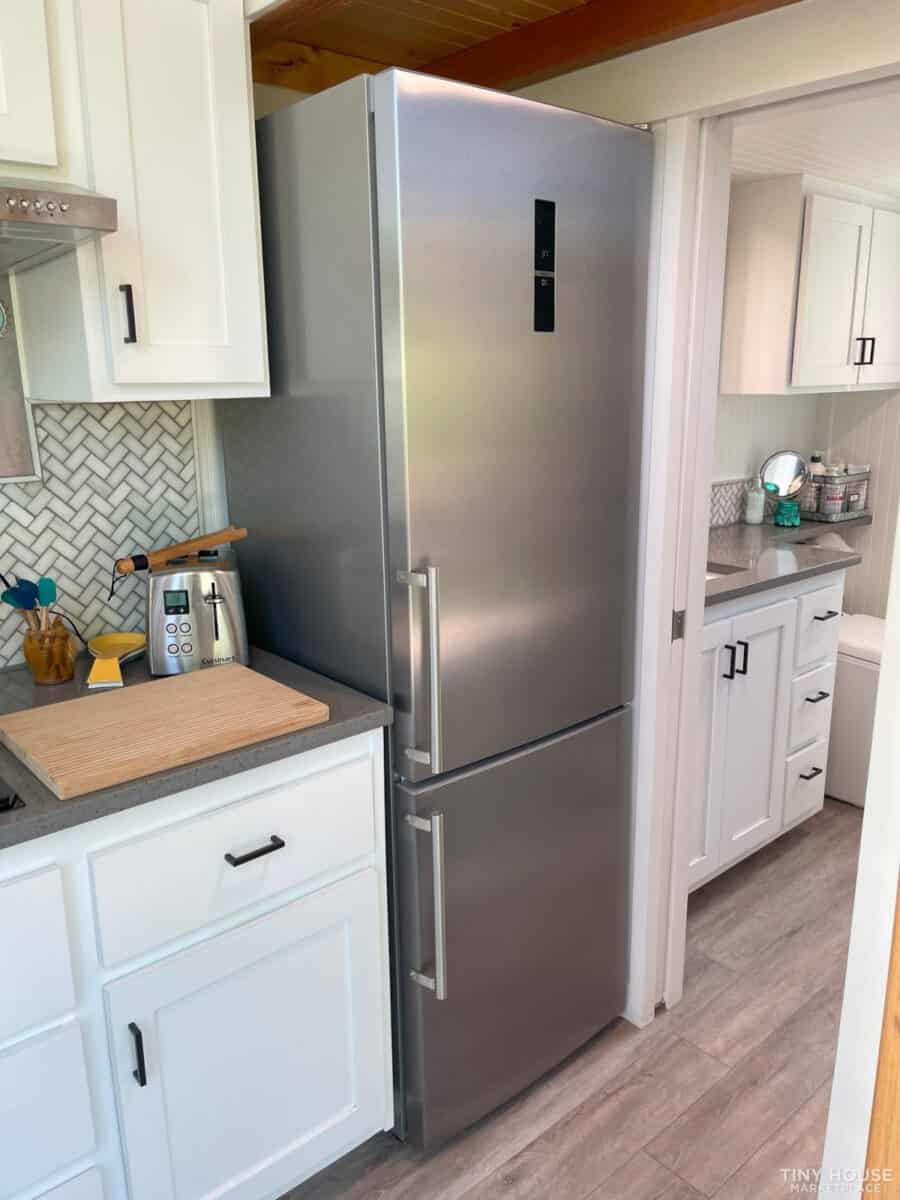 Compact kitchen featuring a stainless steel refrigerator and white cabinetry in a tiny house.