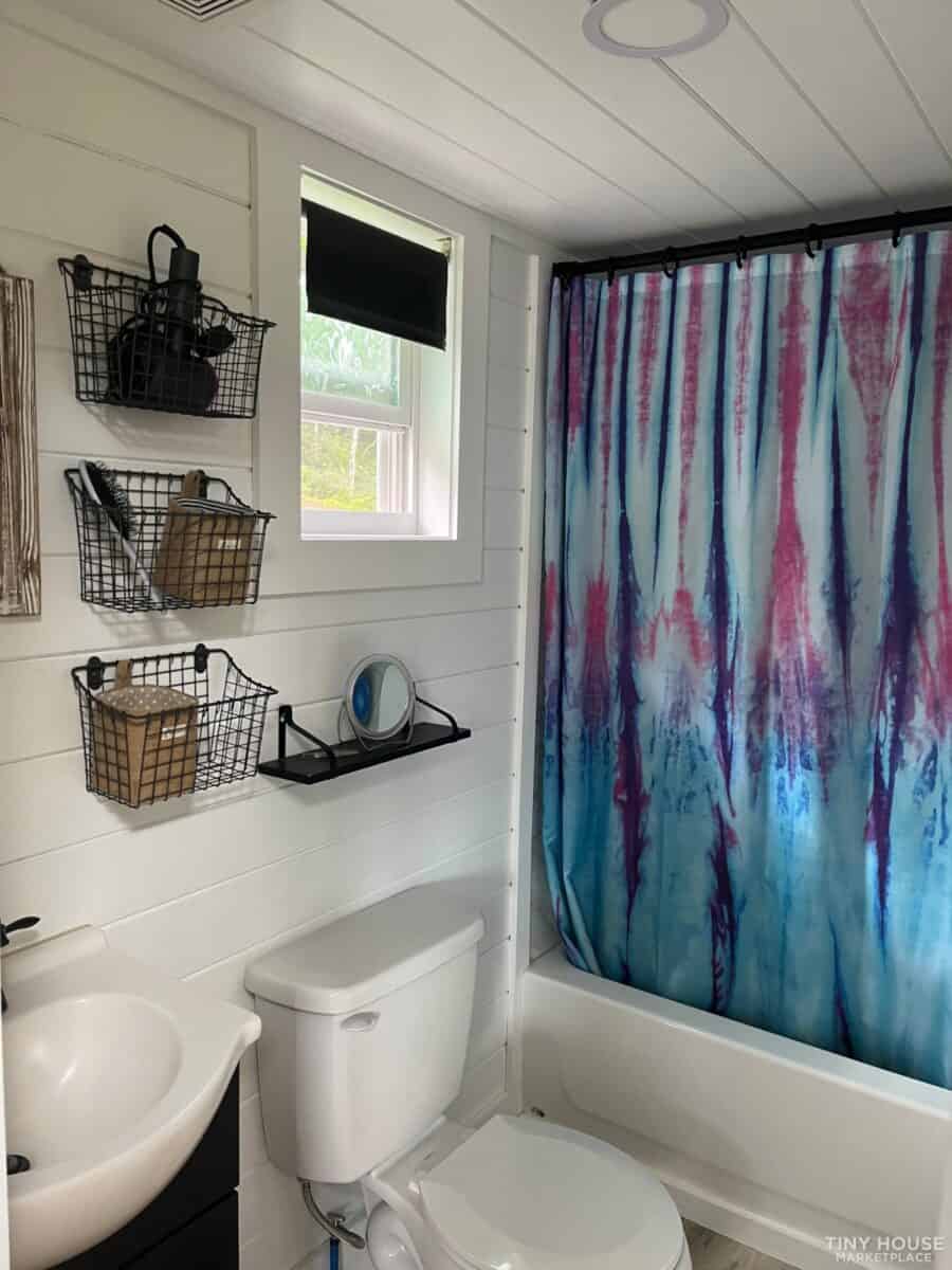 Bright tiny house bathroom featuring a vibrant, artistic shower curtain and efficient space-saving f.