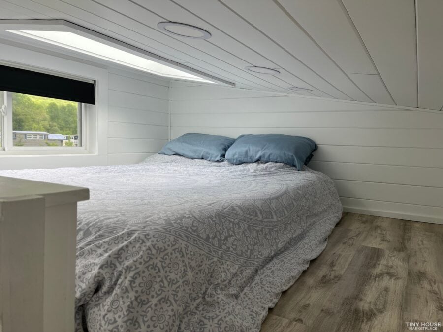 Compact bedroom inside a tiny house with white shiplap walls and a sloped ceiling.