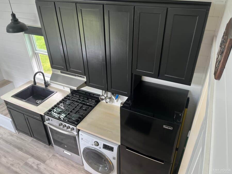 Compact tiny house kitchen with black cabinetry and modern appliances.