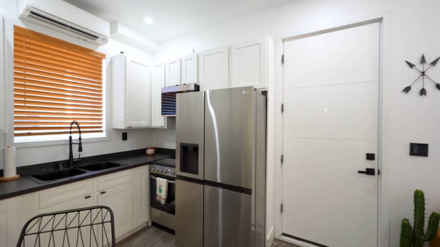 Modern tiny house kitchen with white cabinets and stainless steel appliances.