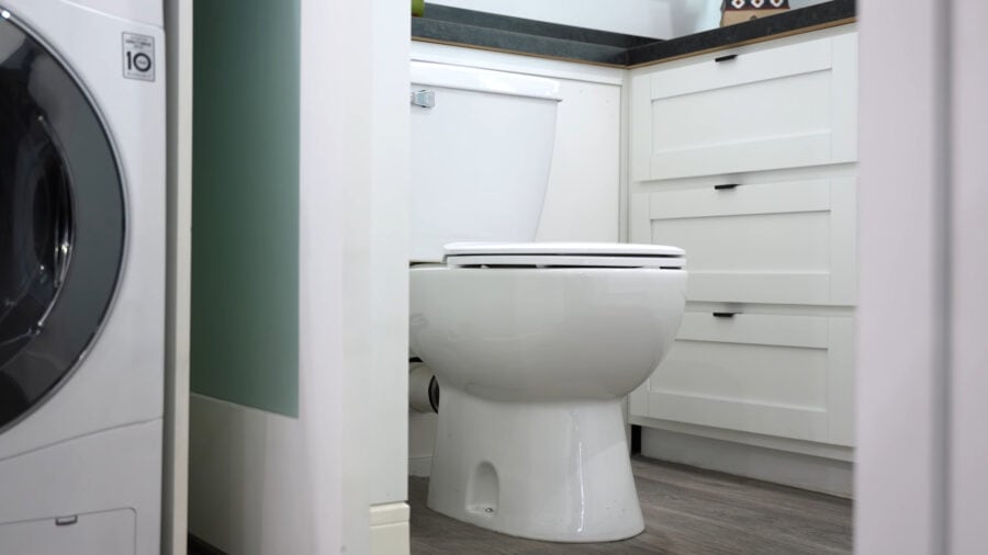 Compact tiny house bathroom with toilet and modern cabinetry.