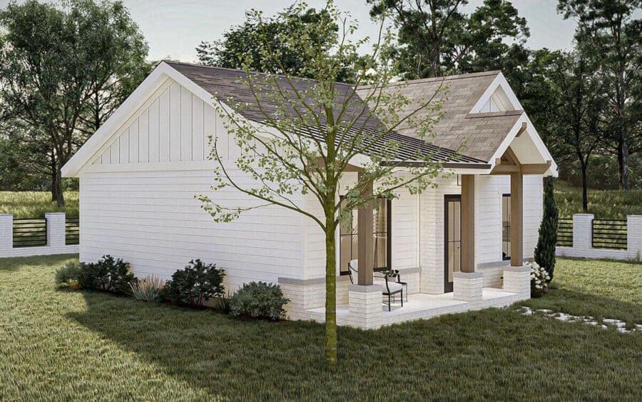Small white cottage with front porch, surrounded by greenery and trees.