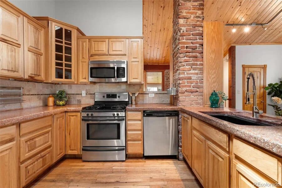 Modern tiny house kitchen with wooden cabinets, stainless steel stove, and granite countertops.