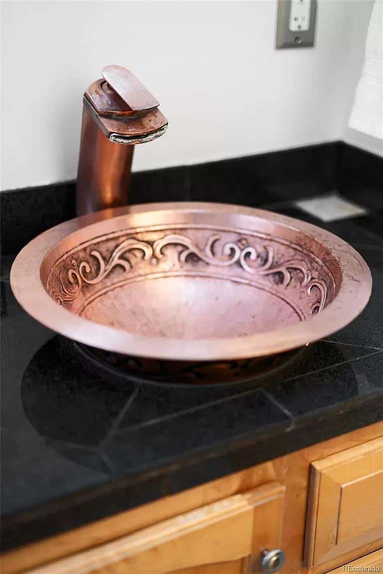 Copper bathroom sink with ornate design and rustic faucet.