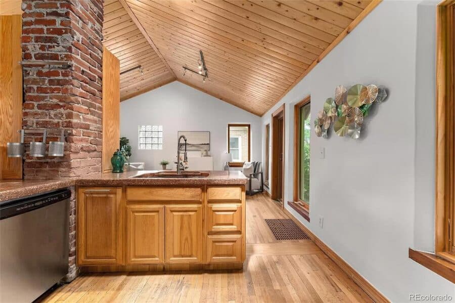 Bright tiny house kitchen with vaulted wooden ceiling and modern appliances.