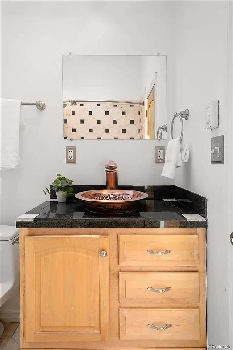 Small bathroom with wooden vanity, copper sink, and modern fixtures in a Spanish-style home.