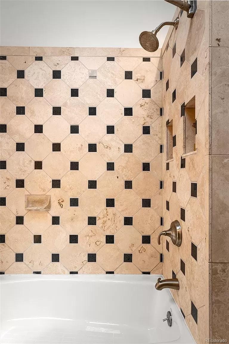 Tile shower with black and beige accents in a compact bathroom.