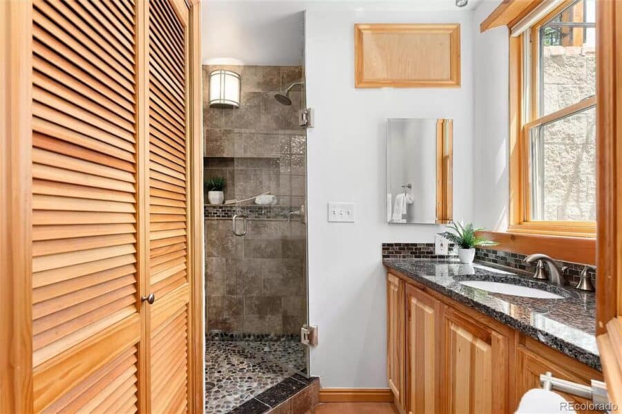 Bright bathroom with walk-in shower and natural wood accents in a compact Spanish-style house.