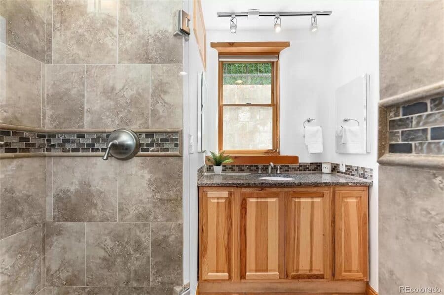 Small bathroom in a tiny house featuring a wooden vanity, tiled walls, and a window for natural ligh.