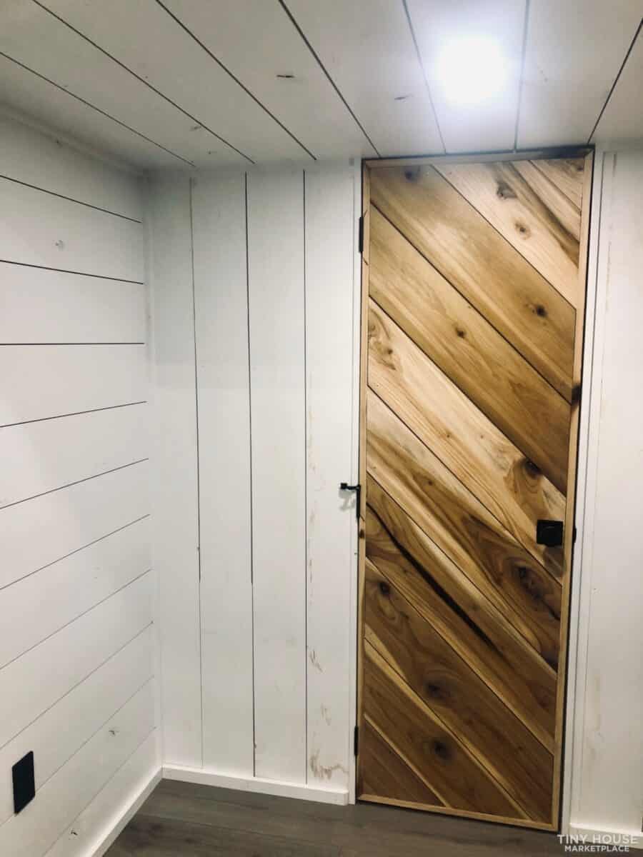 Interior view of a tiny house on wheels with a diagonally patterned cedar wood door.