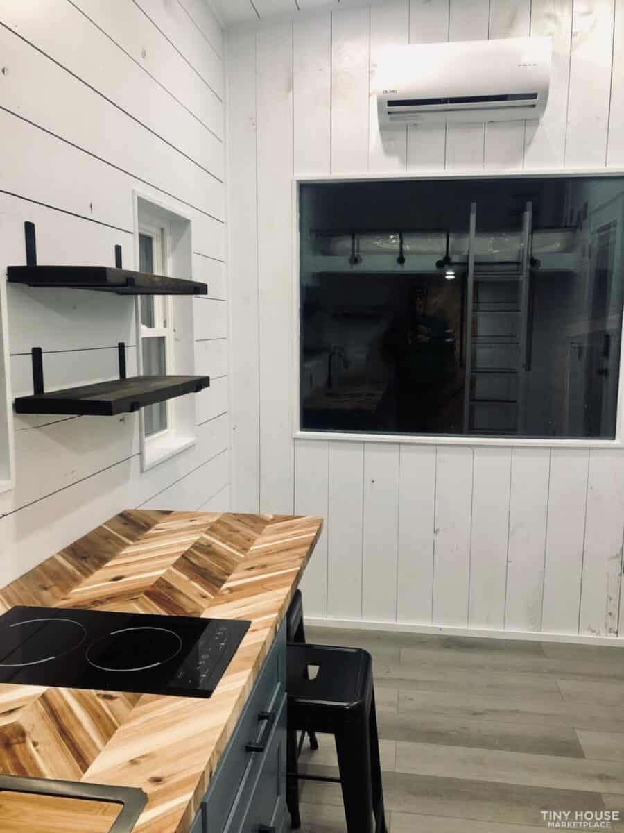 Compact tiny house kitchen with modern appliances and white wood panel walls.