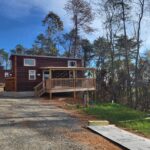 Tiny house with wooden exterior and porch in a wooded setting.