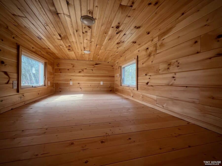 Interior of a tiny house with natural wood walls and ceiling, featuring two windows for natural ligh.