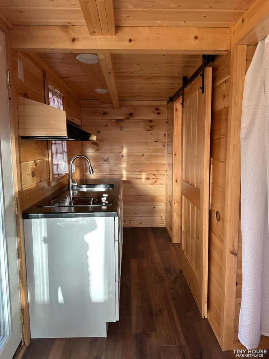 Compact tiny house kitchen with wooden interior and modern appliances.