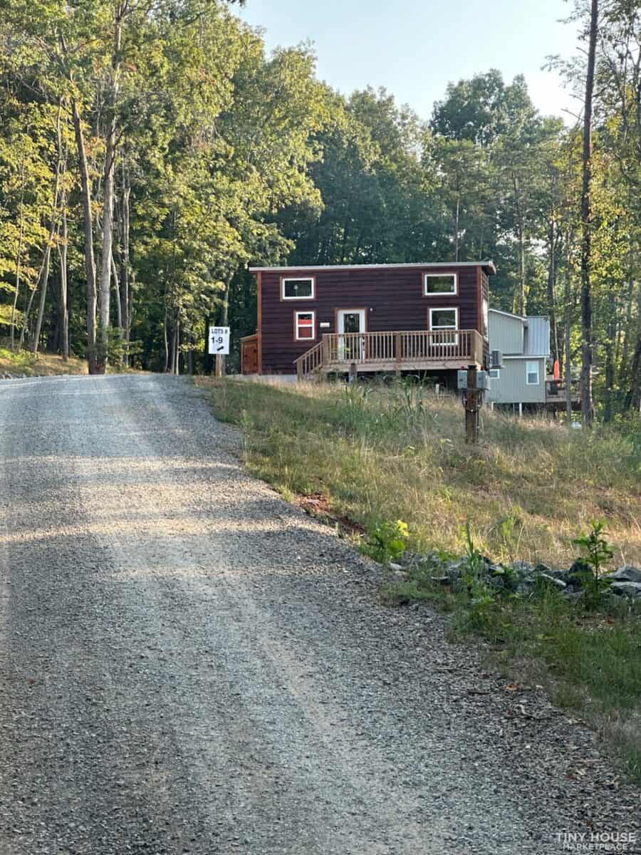 Tiny house with dark exterior and small porch, surrounded by trees.