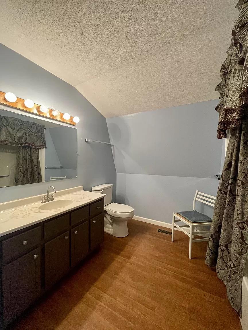 Interior of a tiny A-frame house with a bathroom, wooden floors, and decorative curtains.