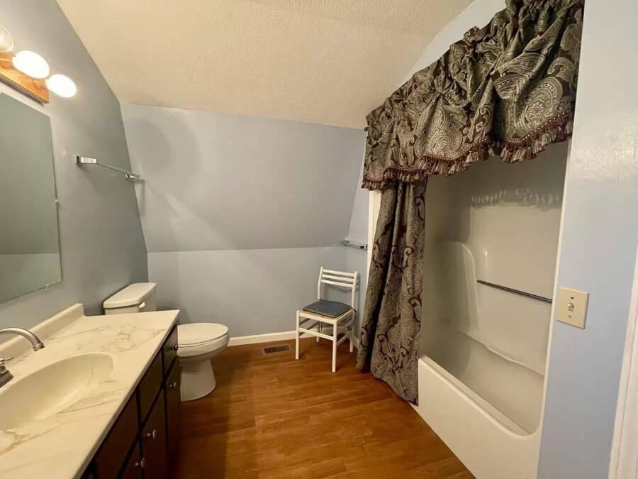 A-Frame tiny house bathroom featuring a bathtub, shower curtain, and compact fixtures.