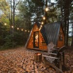 Charming A-frame earth cabin on a Massachusetts farm, surrounded by trees and cozy outdoor lighting.