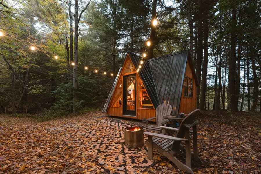 Charming A-frame earth cabin on a Massachusetts farm, surrounded by trees and cozy outdoor lighting.