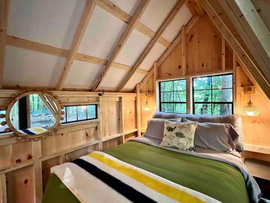 Interior view of a cozy A-frame earth cabin bedroom with wooden walls and large windows.